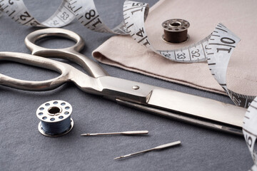 Scissors, spools of thread, needles, and a centimeter lie on the dark gray fabric of the T-shirt. Sewing accessories on the background of sewn clothes. Cutting and sewing concept. Tailor's Desk