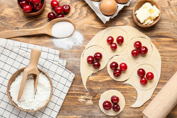 Fresh dough for cherry dumplings and ingredients on wooden background