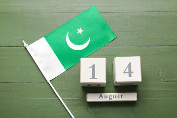 Flag of Pakistan and calendar with date of Independence Day on color wooden background