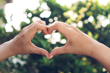 Woman hand do heart shape on green nature bokeh tropical.