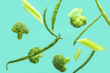 Flying green vegetables on color background