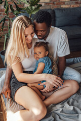 Cheerful little girl with her multiethnic parents on bed