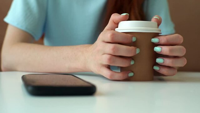 Close-up of unrecognizable nervously woman tapping fingers on cup of coffee while waiting for phone to ring. Closeup hands of stressed female call waiting, sitting at desk. Shooting in slow motion.