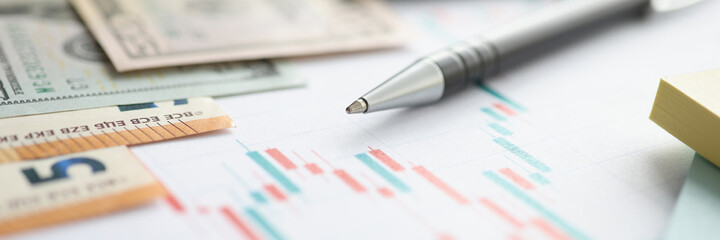 Money and ballpoint pen lying on documents with charts closeup