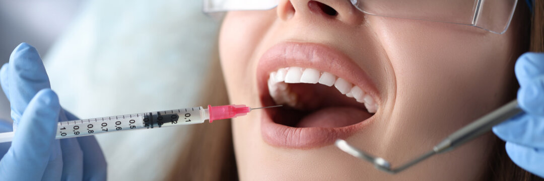 Dentist making injection in gum of female patient in clinic