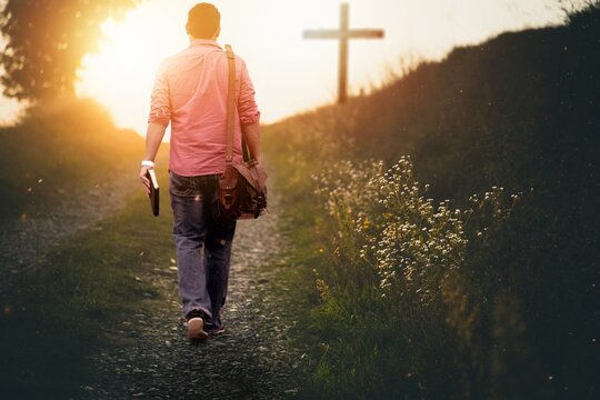 Male holding the bible walking up to the hill towards the cross with a blurred background