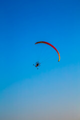 paraglider flying with paramotor on air on evening against the blue sky