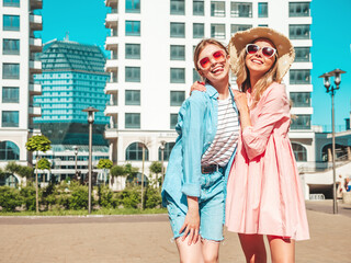 Two young beautiful smiling hipster female in trendy summer clothes and dress.Sexy carefree women posing on the street background. Positive pure models having fun at sunset, hugging and going crazy