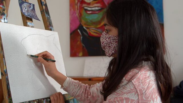 Girl with face mask making a realistic drawing of a leopard in a canvas