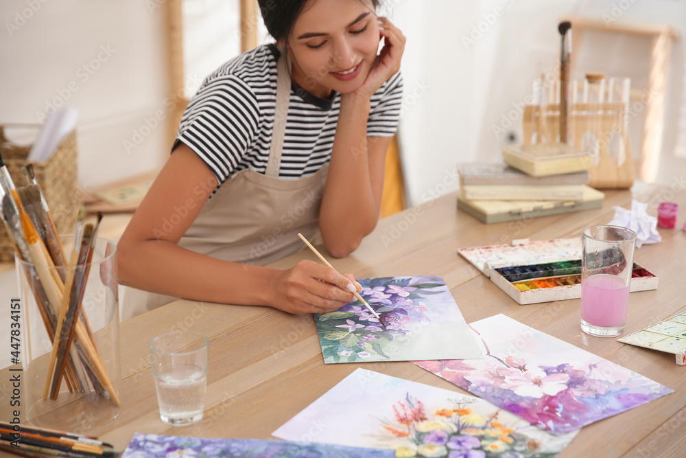 Poster young woman drawing flowers with watercolors at table indoors, focus on painting