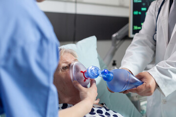 Doctor and nurse helping sick hospitalized senior woman breath, with ambu bag during resustacitor...
