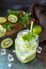 Summer refreshing drink with kiwi, cucumber, lime and ice, mojito or soda with cucumber on a dark stone table.