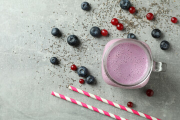 Glass jar of smoothie, ingredients and straws on gray textured table