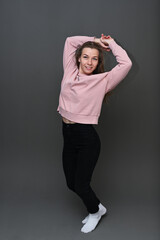 High resolution photo in full growth of a joyful caucasian smiling girl on a gray background in a pink blouse and black trousers.