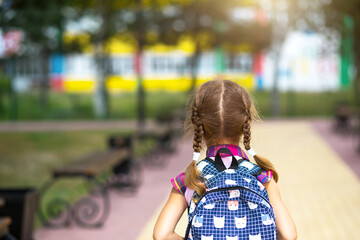 Cheerful girl with a backpack and in a school uniform in the school yard back to the frame. Back to...