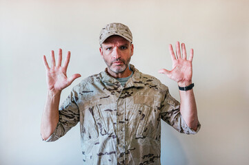 Caucasian man in camouflaged army uniform making stop gesture with hands in hand, expression of...