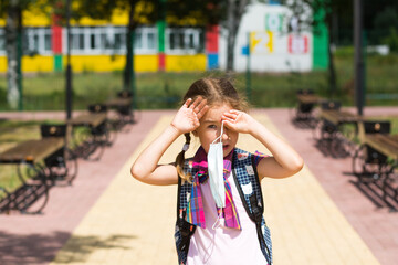 Girl with a backpack near the school after classes takes off a medical mask, unhappy, tired and...