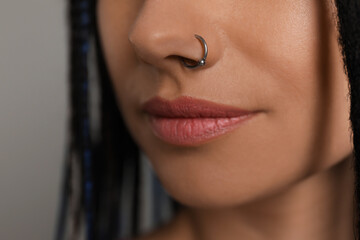 Young woman with nose piercing on grey background, closeup