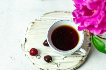 Shabby chic tea. A cup of tea on a white wooden tray with a cherry nearby. Peonies are in a white box. Blurred background