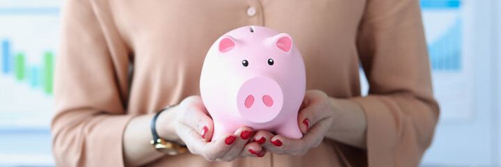 Woman holding pink piggy bank in office closeup