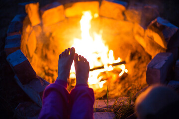 Bare feet of child by fire. Gatherings at night by campfire in open air in summer in nature. Family...