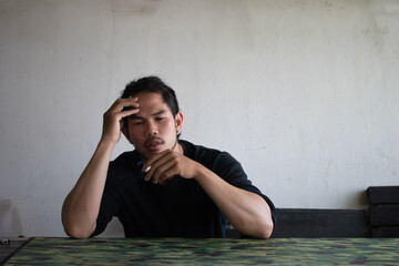 Depressed and hopeless asian man sitting alone after using drugs sitting on the floor. Drugs addiction and withdrawal symptoms concept. - obrazy, fototapety, plakaty