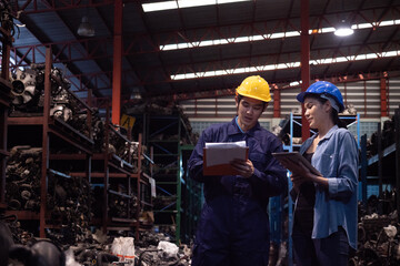 Asian engineer wearing safety helmet holding clipboard with worker in the automotive warehouse.