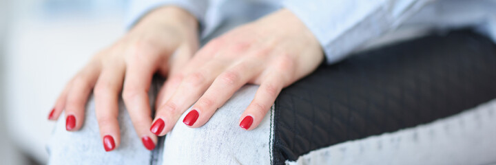 Female hands with red manicure lying on knees closeup