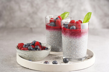 Two glasses with chia seeds pudding, raspberry jam and fresh raspberries and blueberries on a...