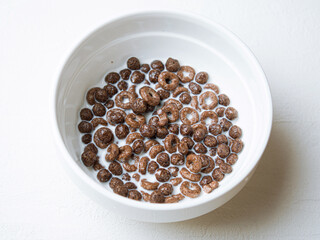 White ceramic plate with chocolate breakfast cereal and milk.