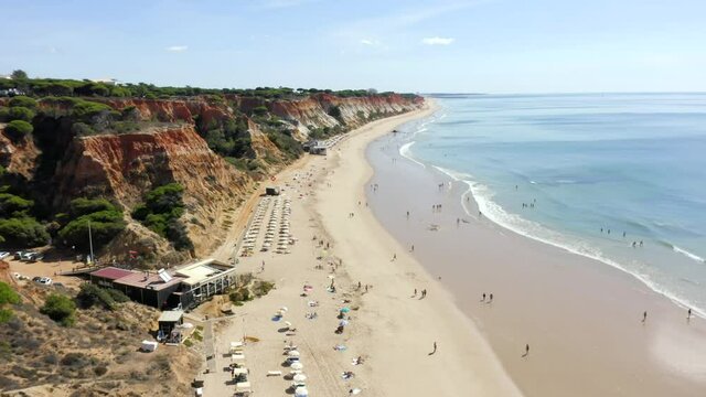 Tourists Enjoying Sandy Beach With Restaurants - Coastal Cliffs And Seascape From Falesia Beach In Algarve, Albufeira, Portugal. - aerial drone