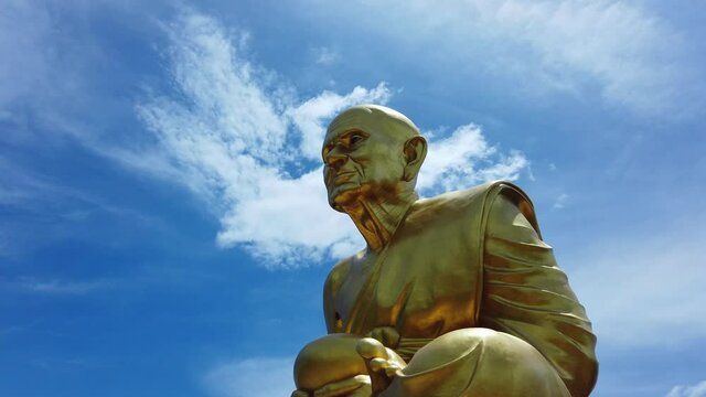 Gigantic golden statue of a Buddhist monk Luang Pu Thuat against beautiful blue sky background with a silhouette of bird flying pass in Phuttha Utthayan Maharat Phra Nakhon Si Ayutthaya, Thailand.