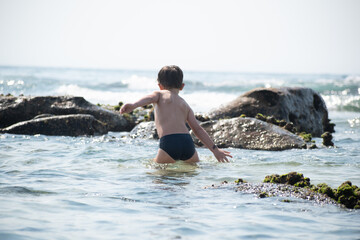 Fototapeta premium Young boy playing in the waves at the beach, in summer.