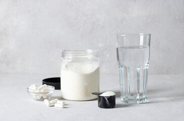 Collagen powder in a jar and measuring spoon, collagen capsules and a glass of water on light gray background. Healthy and antiage concept