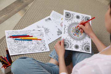 Young woman coloring antistress page on floor, closeup