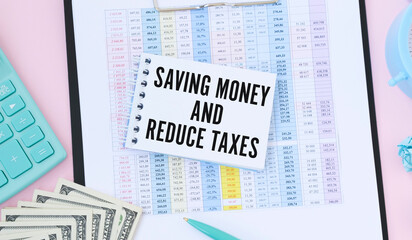 On a light blue background lie black glasses and a pen, a white alarm clock, white paper clips and a notebook with the words SAVING MONEY AND REDUCE TAXES. Business concept