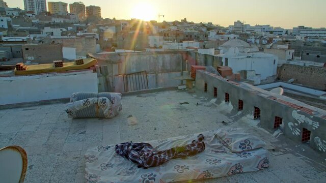 a homeless man stayed on the roof of the house, a mattress and a blanket in the light of the rising sun against the background of the waking city. an image of freedom without money and obligations