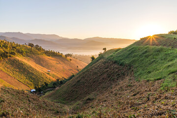 Sunrise in a mountain village with sun rays passing through a foggy hills