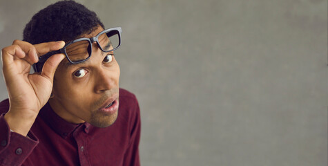 Closeup shot of sceptic black man taking off glasses suspecting you of something and looking at you with emotion of disbelief on face isolated on gray banner background with blank copy space for text - obrazy, fototapety, plakaty