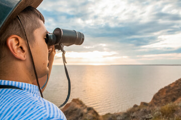 Obraz premium a man on a high hill at the sea looks through binoculars in the summer