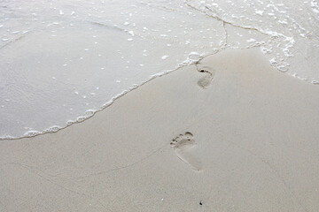 Sea water coming on the white beach sand with footprint