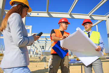 Female architect, construction engineer and manager talking about the project on construction site. Teamwork and people concept - group of builders and architect in hardhats