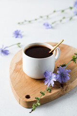 Fototapeta na wymiar Chicory drink in a white mug with chicory flowers next to it on a wooden board.