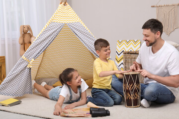 Father and children playing near toy wigwam at home © New Africa