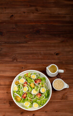 Big white bowl of lettuce, sprout salad with boil egg, onion and tomato mixed with Japanese sesame oil dressing on brown wooden table together with small olive oil jar and sesame cup