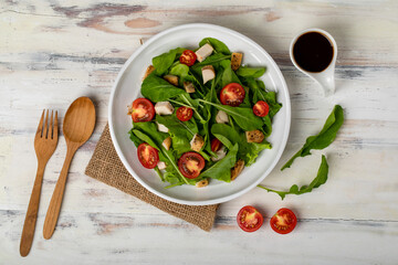  Fresh spinach salad with tomato, small pieces of herb roasted chicken in white ceramic dish on brown sack cloth on white wooded table. Concept for healthy