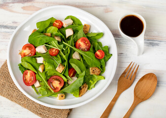 Fresh spinach salad with tomato, small pieces of herb roasted chicken in white ceramic dish on brown sack cloth on white wooded table. Concept for healthy