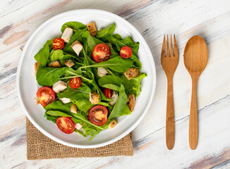 Fresh spinach salad with tomato, small pieces of herb roasted chicken in white ceramic dish on brown sack cloth on white wooded table. Concept for healthy