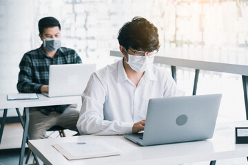 Asian colleague works while wearing a mask in the office during COVID-19.
