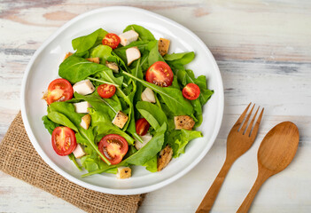 Fresh spinach salad with tomato, small pieces of herb roasted chicken in white ceramic dish on brown sack cloth on white wooded table. Concept for healthy
